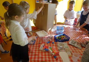 Grupa dzieci dekoruje karton papierowy kolorowymi ścinkami papieru.